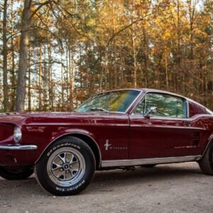 Ford Mustang Fastback clásico de 1967 en vista diagonal exterior, con carrocería roja, techo fastback, llantas y perfil deportivo.